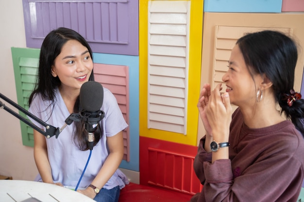 Duas mulheres asiáticas brincando com gestos de mãos usando o microfone durante o podcast