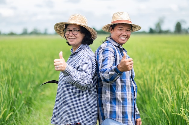 Duas mulheres asiáticas de fazendeiras tailandesas vestem uma camisa azul sorrindo e com o polegar levantado na fazenda verde