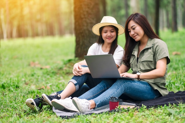 Duas mulheres asiáticas trabalhando e usando um laptop enquanto estão sentadas no parque