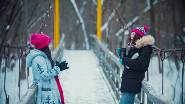 Duas mulheres bebendo bebidas quentes da garrafa térmica e caminham na ponte