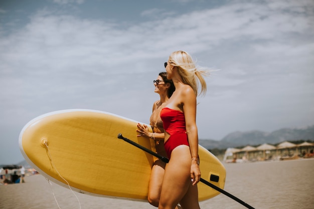 Duas mulheres bonitas com prancha de remo na praia em um dia de verão