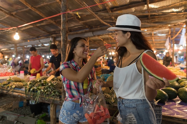 Foto duas mulheres bonitas, degustação de melancia no mercado de rua tradicional na ásia