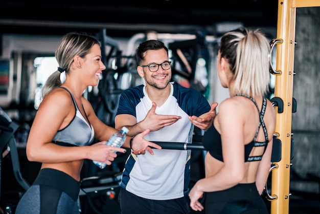 Duas mulheres bonitas dos esportes do ajuste que falam com um indivíduo considerável no gym.