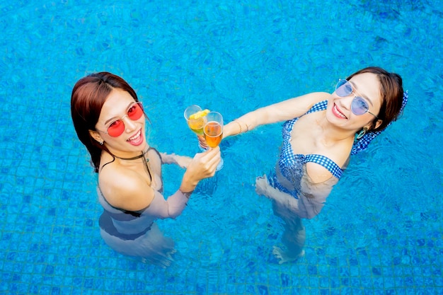 Duas mulheres brindam com taças de vinho na piscina