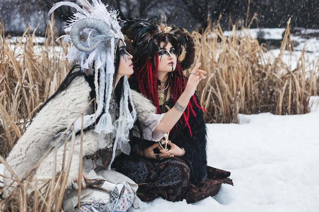 duas mulheres bruxas em roupas de fantasia e coroas sentadas na neve do inverno