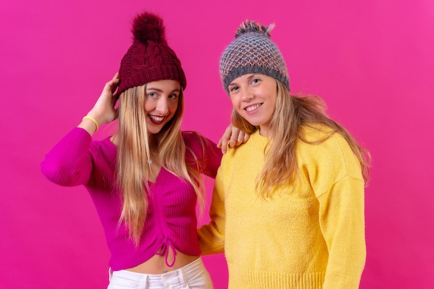 Duas mulheres caucasianas loiras com chapéus de lã em um retrato de fundo rosa olhando