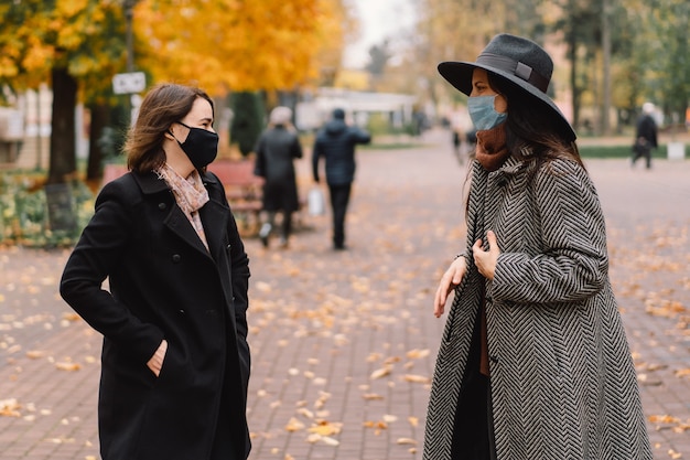 Duas mulheres com máscaras protetoras caminham no parque e mantêm uma distância social