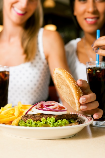 Foto duas mulheres comendo hambúrguer e bebendo refrigerante