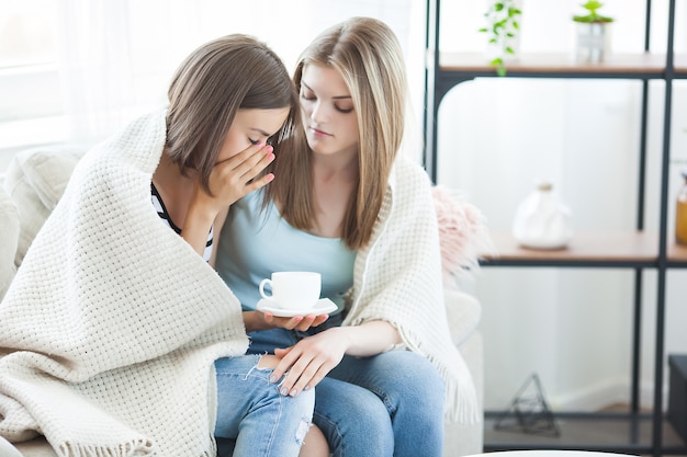 Duas mulheres conversando no sofá dentro de casa.