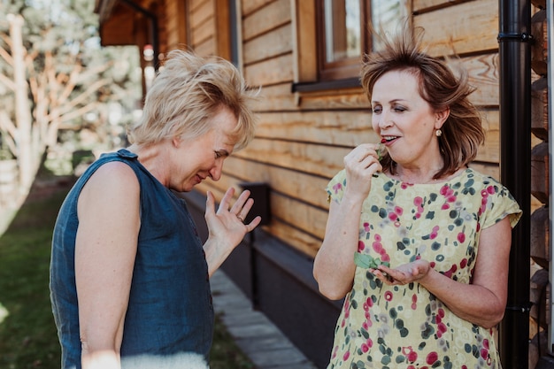 Duas mulheres de 55 anos falando fofinho no fundo de uma parede de madeira