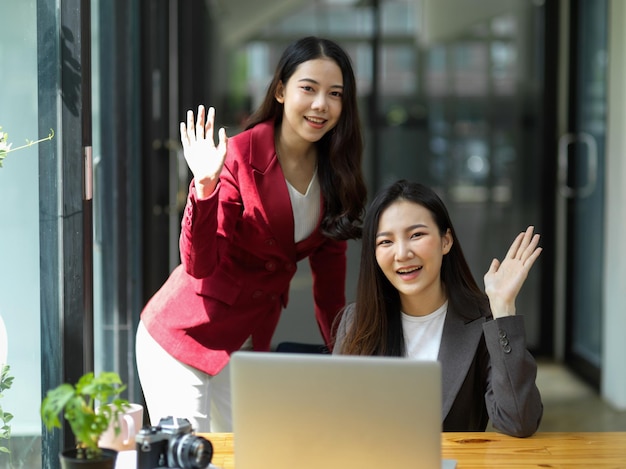 Duas mulheres de negócios amigáveis felizes cumprimentando com a mão o gesto para a câmera no escritório.