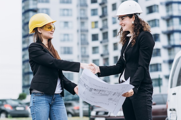 Duas mulheres de negócios em capacetes de proteção e óculos de segurança que procuram esquemas de construção, conceito arquitetônico
