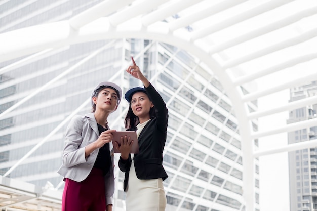 Duas mulheres de negócios, engenheiros industriais em pé na frente do prédio com planta na mão