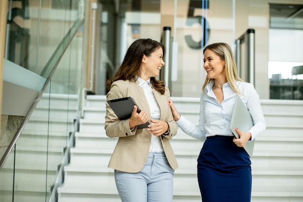 Duas mulheres de negócios jovens andando nas escadas no corredor do escritório