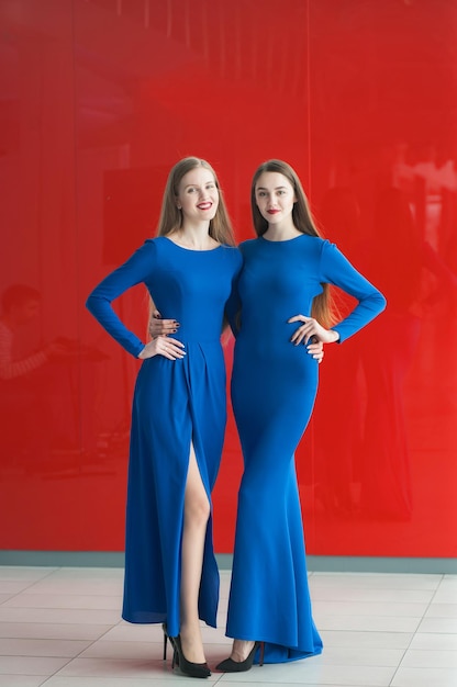 Duas mulheres de vestido azul sobre fundo vermelho