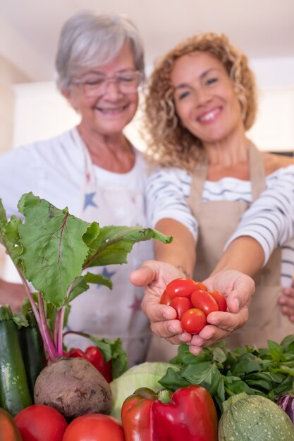 Duas mulheres desfocadas na cozinha em casa segurando nas mãos pequenos tomates vermelhos. Crua fresca colhida na mesa