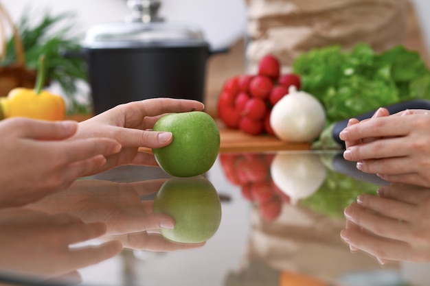 Duas mulheres discutindo um novo menu na cozinha, close-up. Mãos humanas de duas pessoas gesticulando na mesa entre legumes frescos. Conceito de culinária e amizade.