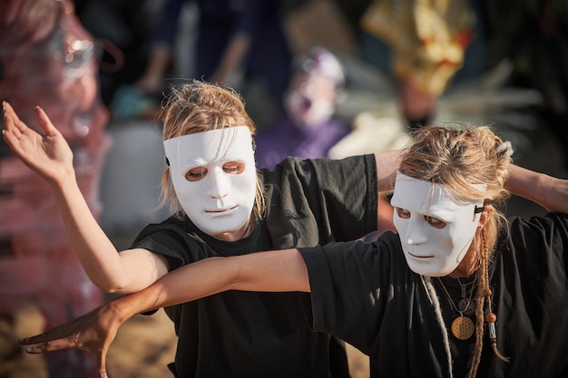 Duas mulheres em máscara de teatro branco dançando no festival de arte teatral performance de dança ao ar livre de duas meninas dançarinas em estilo de roupa preta total festival de performance teatral de arte ao ar livre