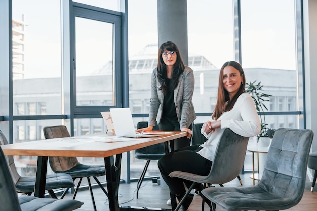 Duas mulheres em roupas formais estão dentro de casa no escritório moderno trabalham juntas