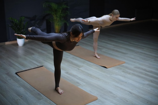 Duas mulheres esportivas praticando ioga no estúdio em pé em uma perna e se exercitando.