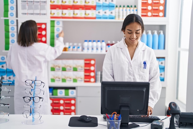 Duas mulheres farmacêuticas usando computador trabalhando na farmácia