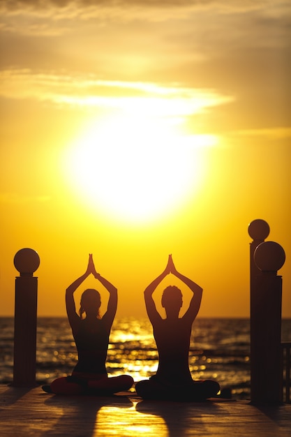 Duas mulheres fazem ioga ao nascer do sol perto do mar