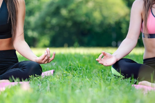 Duas mulheres fazendo meditação de ioga em uma pose de lótus ao ar livre em um parque em um dia ensolarado no espaço de cópia fechada