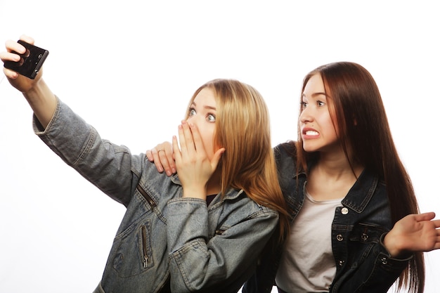 Duas mulheres fazendo selfie com o celular, isolado no branco