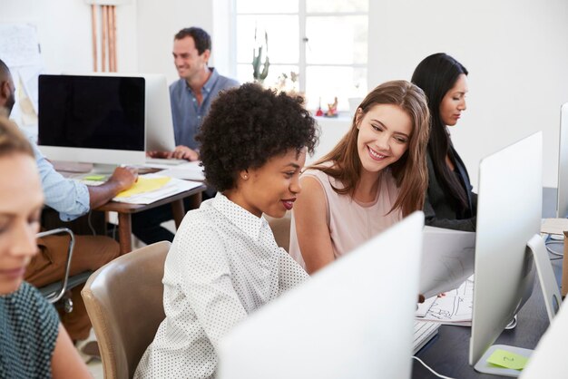 Duas mulheres felizes discutem o trabalho no computador no escritório de plano aberto