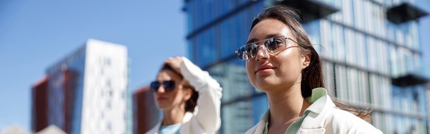 Duas mulheres felizes em roupas da moda riem e caminham para fora no fundo de edifícios modernos