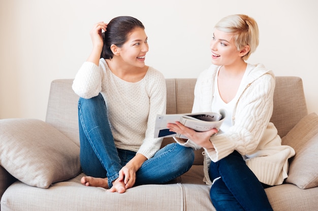 Duas mulheres felizes lendo revista no sofá em casa