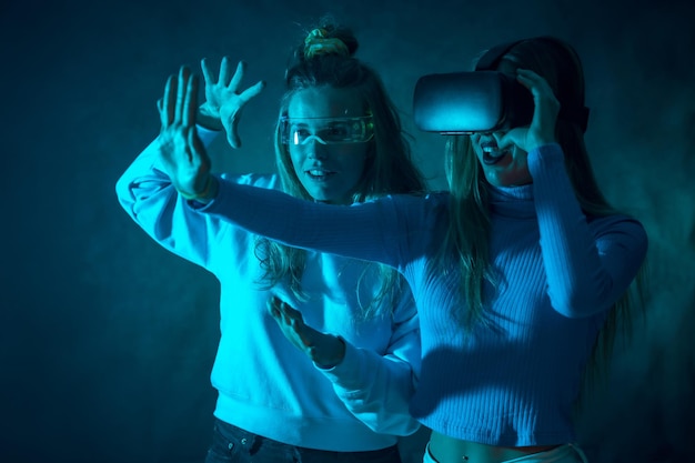 Duas mulheres futuristas em óculos vr jogando um jogo de realidade virtual fundo azul