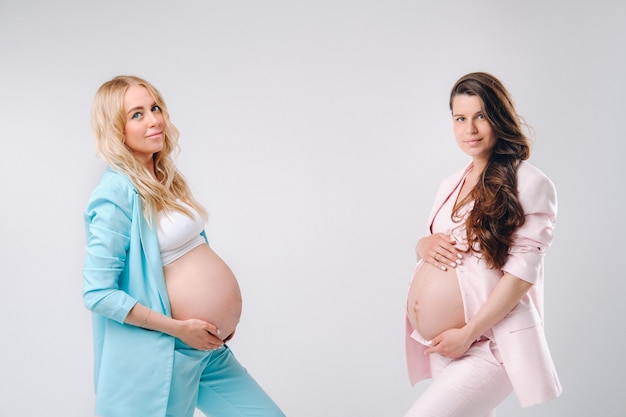 Duas mulheres grávidas com barrigas grandes em ternos em um fundo cinza.