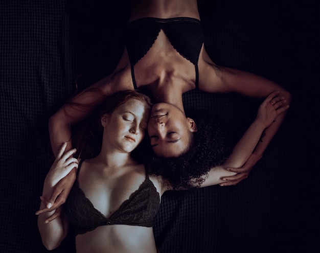 Duas mulheres homossexuais em lingerie mentindo de olhos fechados na cama. Lésbicas multirraciais relaxando na cama, imagem sombria e mal-humorada.