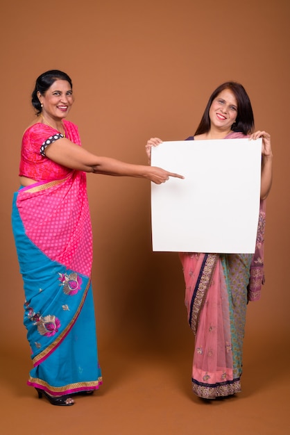 duas mulheres indianas maduras vestindo roupas tradicionais indianas sari junto com um quadro branco