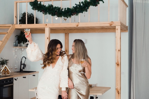 Duas mulheres jovens celebrando o ano novo ou aniversário dentro de casa com taças de vinho