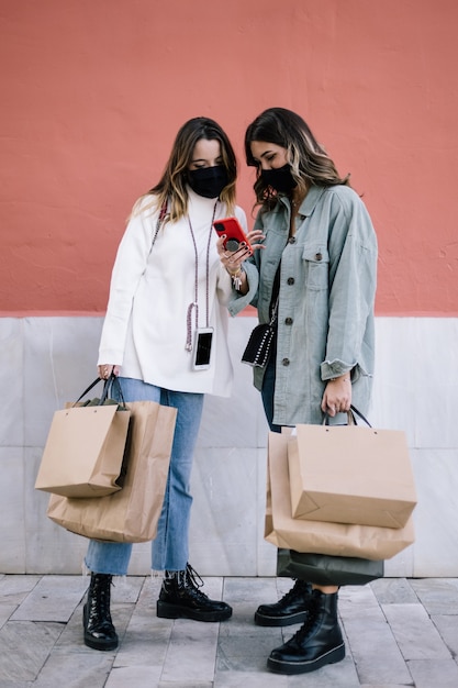 duas mulheres jovens com máscaras, olhando para o celular.