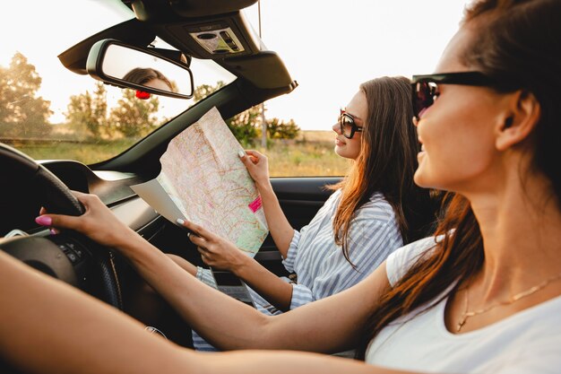 Duas mulheres jovens de cabelos escuros em óculos de sol estão sentadas em um cabriolet preto em um dia ensolarado. Uma delas mantém o mapa nas mãos. .