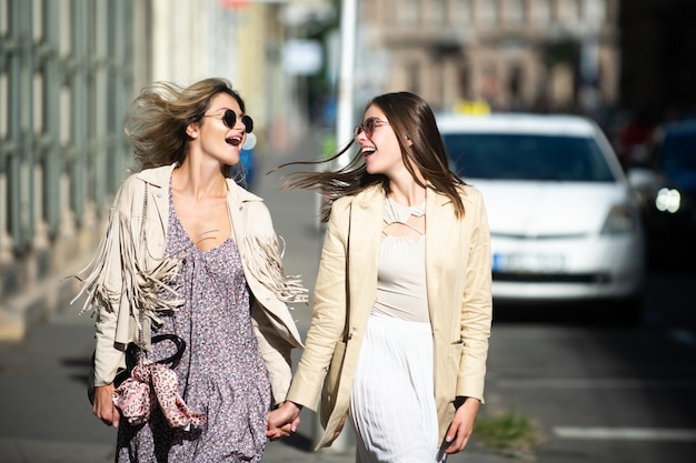 Duas mulheres jovens de lançamento com óculos de sol andando na cidade férias engraçadas viagens românticas