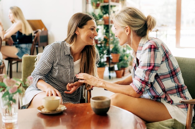 Duas mulheres jovens e magras sentadas numa cafeteria a divertir-se a conversar.