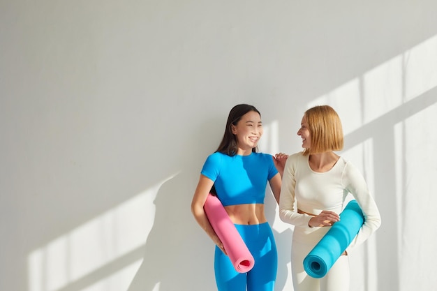 Foto duas mulheres jovens estão na aula de ioga sorrindo e falando