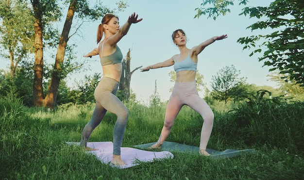 Duas mulheres jovens fazendo ioga virabhadrasana ao ar livre