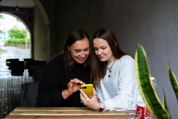 Duas mulheres jovens se comunicam e olham para smartphone no café no terraço