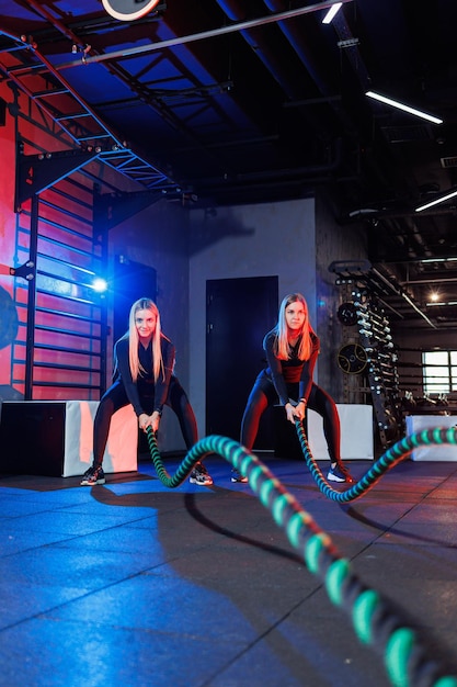 Duas mulheres jovens se exercitando com cordas no ginásio. Mulher fazendo exercícios de corda junto com o treinador