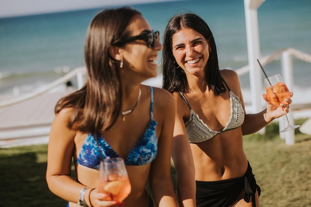 Duas mulheres jovens sorridente em biquíni desfrutando de férias na praia enquanto bebem coquetel