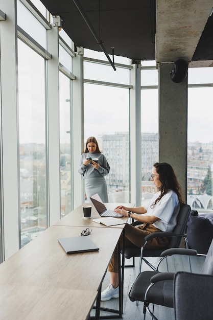 Duas mulheres jovens trabalham em um escritório moderno Espaço de escritório de trabalho com grandes janelas Mulher gerente trabalha na mesa sentada no escritório