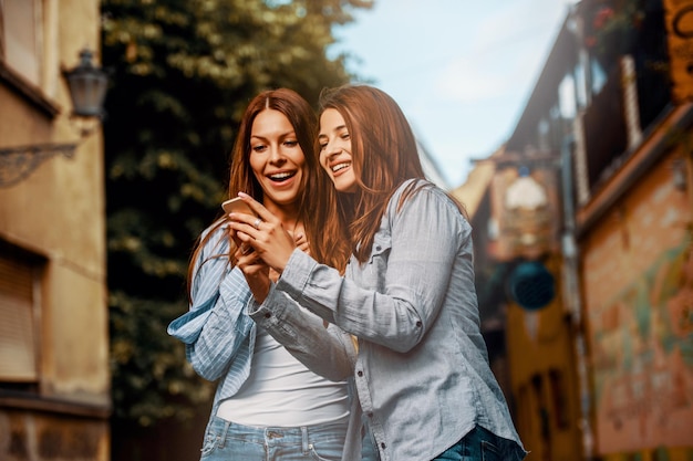 Duas mulheres jovens usando telefone inteligente na rua