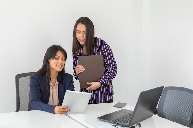 Duas mulheres latinas revisam um projeto em seu tablet enquanto trabalham em um escritório Duas mulheres de negócios trabalhando no escritório