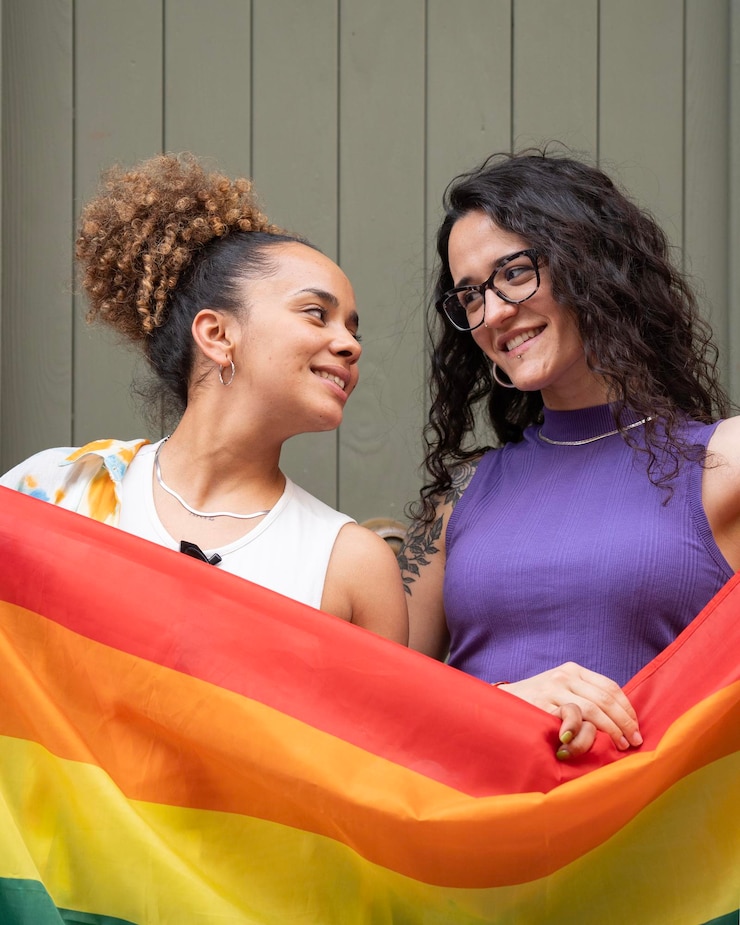 Foto duas mulheres lésbicas sorridente estão segurando uma bandeira arco-íris representando a comunidade lgbtq