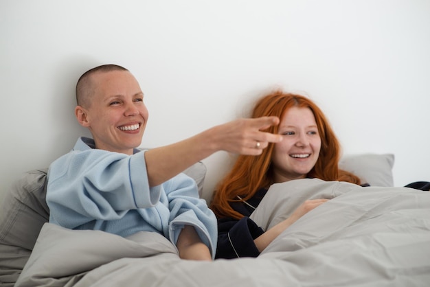 Duas mulheres lísbicas rindo felizes assistindo tv na cama Interação alegre relaxamento